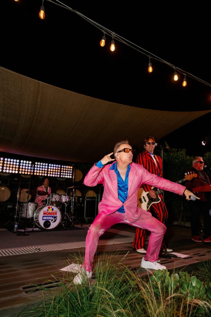 Band performing energetically in vibrant outfits onstage.